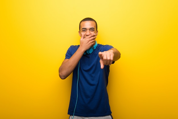 Afroamerikanermann mit blauem T-Shirt auf gelbem Hintergrund zeigend mit dem Finger