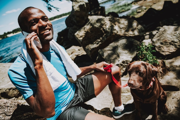 Afroamerikanermann mit Hund sprechend am Telefon