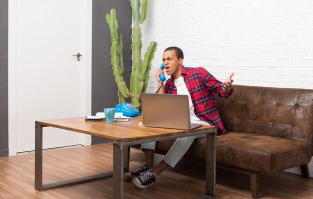 Foto afroamerikanermann mit laptop im wohnzimmer sprechend mit weinlesetelefon