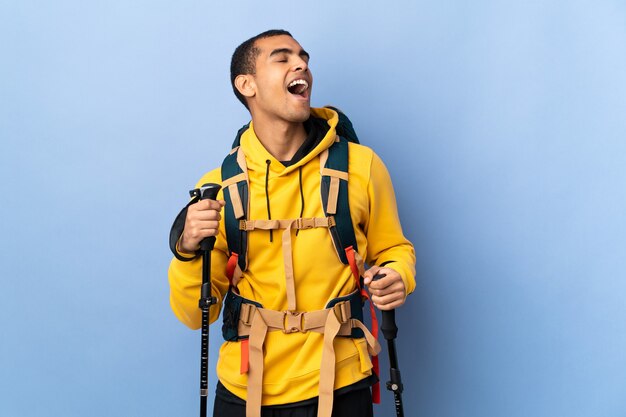 Afroamerikanermann mit Rucksack und Trekkingstöcken über isoliertem Hintergrundlachen