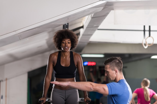 afroamerikanische Athletin trainiert die Arme auf Dips horizontalen Barren Trainieren Sie Trizeps und Bizeps und machen Sie Liegestütze mit dem Trainer