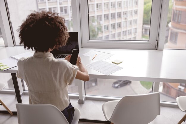 Afroamerikanische Dame, die mit ihrem Smartphone und Laptop arbeitet