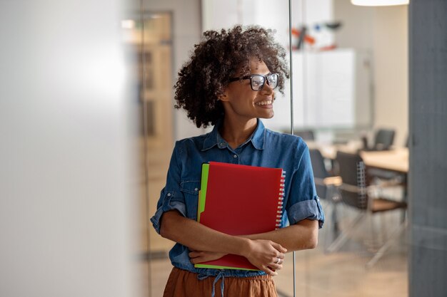 Afroamerikanische Dame mit Brille posiert mit Ordnern