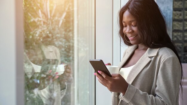 Afroamerikanische Dame trinkt Kaffee und SMS am Telefon