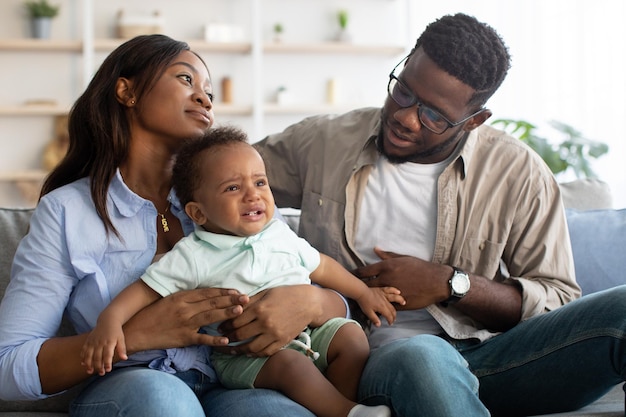 Afroamerikanische Eltern trösten weinendes Kind auf dem Sofa