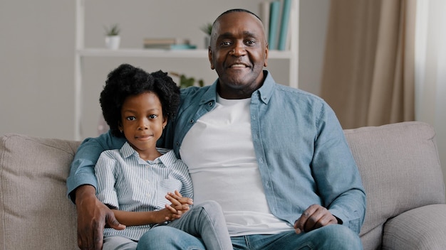 Afroamerikanische Familie, die auf dem Sofa sitzt, Kind, Mädchen, winkt, hallo grüßend, erwachsener Vater, der Tochter umarmt