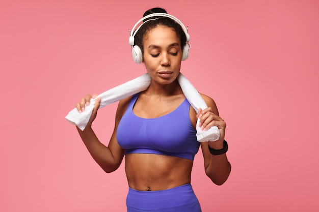 Afroamerikanische Fitnessdame mit Tracker und Kopfhörern rosa Hintergrund