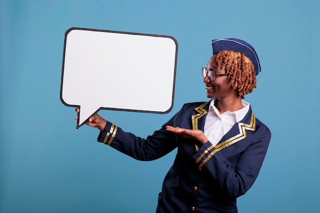 Afroamerikanische Flugbegleiterin mit Sprechblase. Lächelndes Stewardess-Studioporträt mit Banner neben ihr. Uniformierte Stewardess mit Dialogfenster.