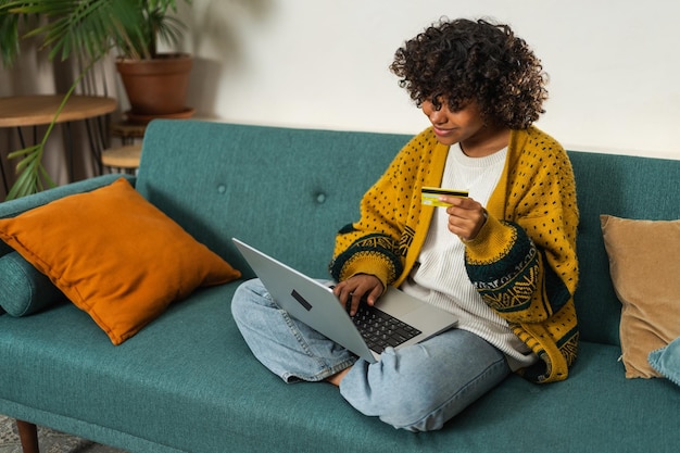 Afroamerikanische Frau benutzt Laptop, macht Online-Shopping, bezahlt mit einer Gold-Kreditkarte.