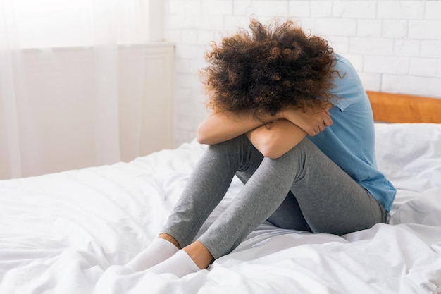Afroamerikanische Frau, die an Depressionen leidet, sitzt auf dem Bett