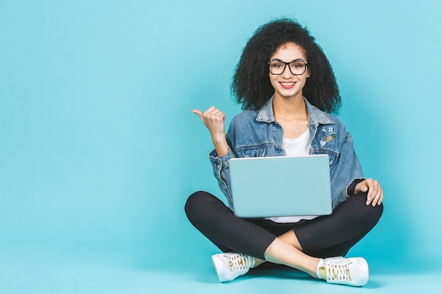 Afroamerikanische Frau, die Laptop benutzt, während sie auf einem Boden mit gekreuzten Beinen sitzt