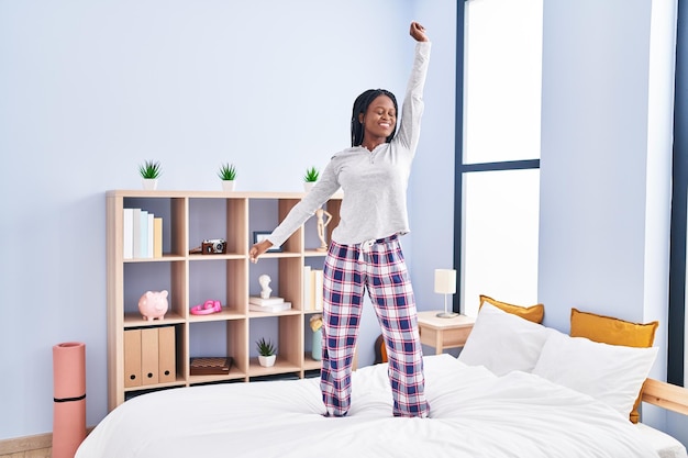 Afroamerikanische Frau lächelt selbstbewusst und tanzt auf dem Bett im Schlafzimmer