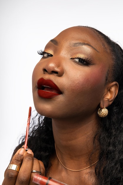 Afroamerikanische Frau macht Make-up und hält Glanzlipstick isoliert auf weißem Hintergrund Schönheit