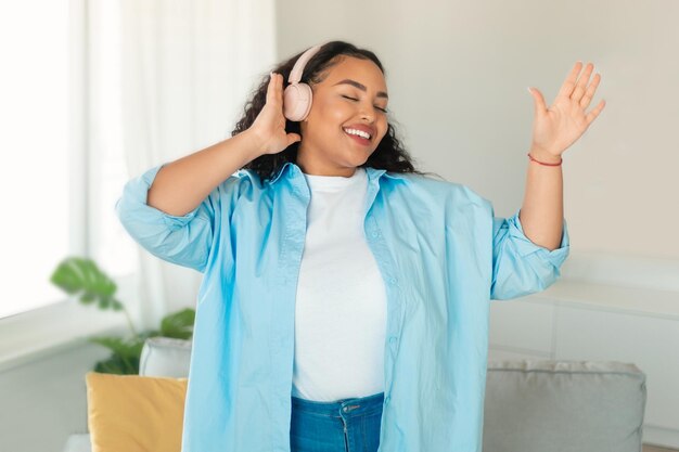 Afroamerikanische Frau mit Kopfhörern, die zu Hause Musik hört und tanzt