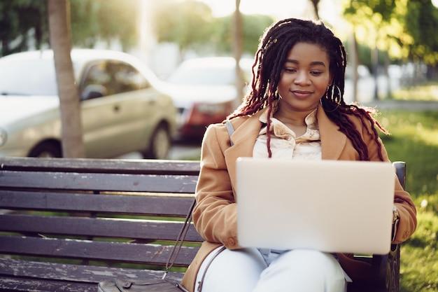 Afroamerikanische Freiberuflerin, die auf einer Bank in einer Straße sitzt und einen Laptop benutzt