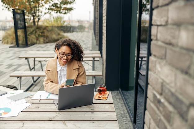 Afroamerikanische Freiberuflerin, die remote arbeitet, während sie auf der Caféterrasse sitzt