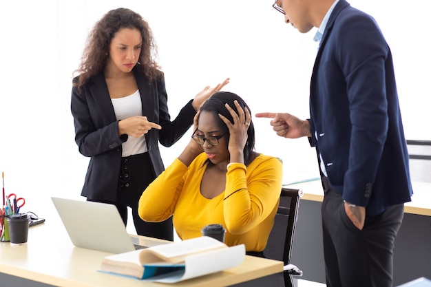 Afroamerikanische Geschäftsfrau verärgerte schwere Fehler und schlechte Arbeit. Kollegen von Männern und Frauen schikanieren und beschuldigen weibliche Mitarbeiter, die mit dem Finger auf sie zeigen