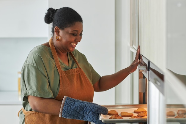 Afroamerikanische Hausfrau holt in der Küche ein Tablett mit Keksen aus dem Ofen