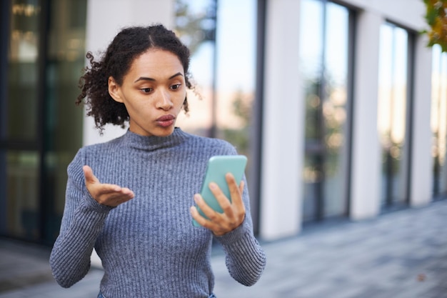 Afroamerikanische junge Frau, die per Videolink auf dem Handy spricht, während sie die Straße entlang geht