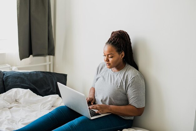 Afroamerikanische junge Frau mit Laptop auf Betttechnologien und Kommunikation und sozialem Netzwerk