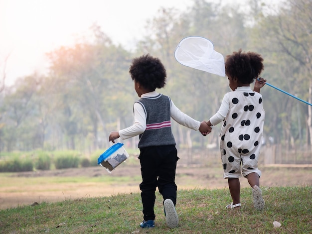 Afroamerikanische Jungen und Mädchen fangen Insekten im Wald auf Abenteuer-Camping-Reisen Vorschulkinder fangen Käfer mit Netz Abenteuer-Kindergarten-Tagesausflug in die wilde NaturxAxA