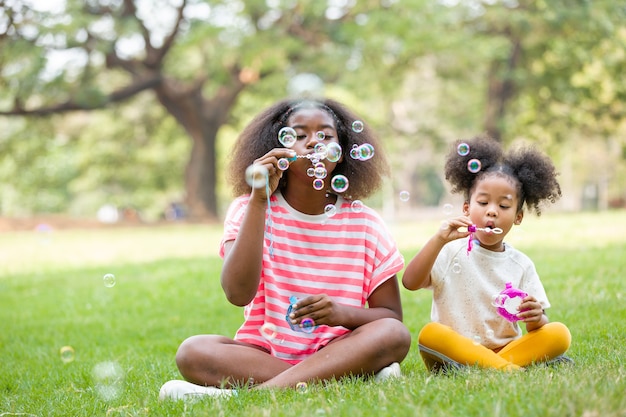 Afroamerikanische Kinder, die mit Seifenblasen im Stadtpark am Feiertagssommertag genießen.