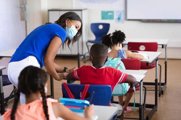 Afroamerikanische Lehrerin mit Gesichtsmaske unterrichtet afroamerikanischen Jungen im Unterricht in der Schule