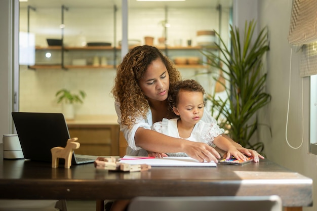 Afroamerikanische Mutter trägt lässige Kleidung und arbeitet in ihrem Haus, während ihre Tochter