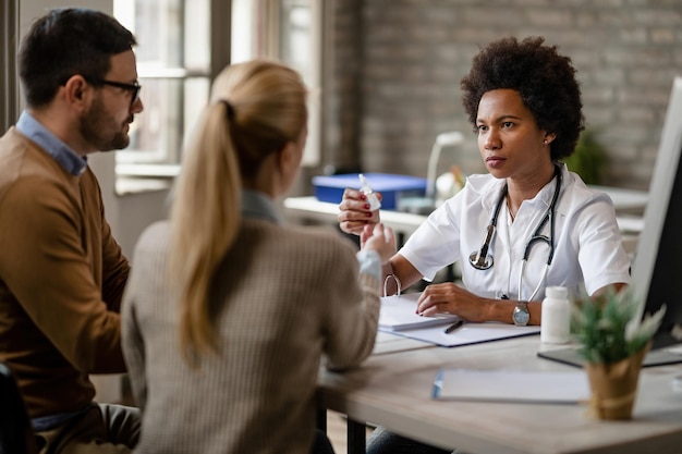 Afroamerikanische Ärztin berät ein Paar über die Einnahme von Medikamenten während eines Treffens in der Klinik