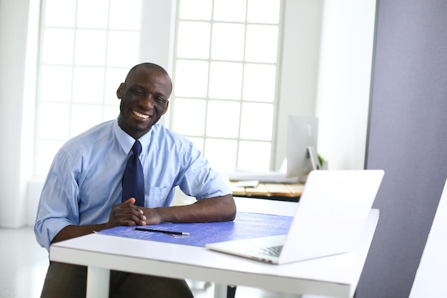 Afroamerikanischer Architekt, der mit Computer und Blaupausen im Büro arbeitet