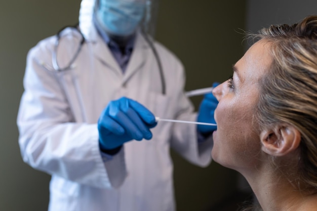 Afroamerikanischer Arzt mit Gesichtsmaske, der einer Patientin einen Covid-Abstrichtest gibt
