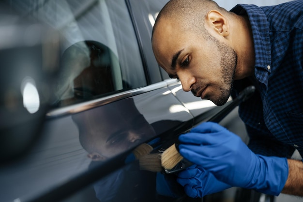 Afroamerikanischer Autoservice-Mitarbeiter, der eine Nanobeschichtung auf ein Auto aufträgt