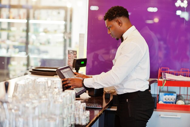 Afroamerikanischer Barkeeper trägt Fliege mit Cash-Terminal-Bildschirm an der Bar