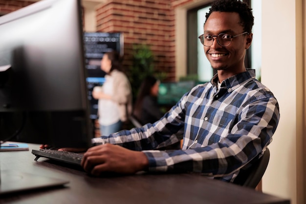 Afroamerikanischer Entwickler, der an einem Softwareprogramm in seiner Programmieragentur arbeitet und Fähigkeiten in Codierung und Technologie nutzt, um ein umfassenderes Programm zu erstellen. Webprogrammierer, der HTML-Skript schreibt