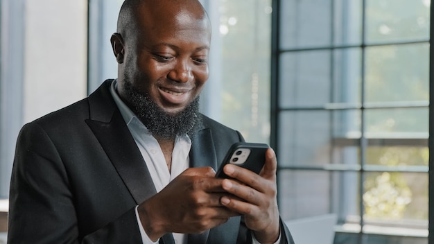 Afroamerikanischer erwachsener Geschäftsmann, bärtiger männlicher Angestellter, der in der Handy-App chattet, halten Mobiltelefon