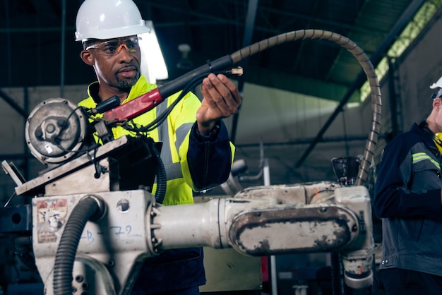 Afroamerikanischer Fabrikarbeiter, der mit einem geschickten Roboterarm arbeitet