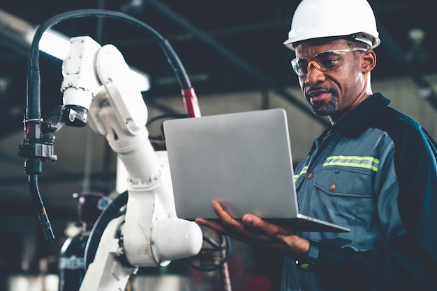 Afroamerikanischer Fabrikarbeiter, der mit einem geschickten Roboterarm arbeitet