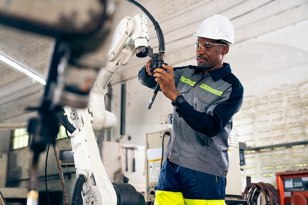 Afroamerikanischer Fabrikarbeiter, der mit einem geschickten Roboterarm arbeitet