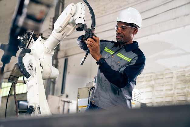 Afroamerikanischer Fabrikarbeiter, der mit einem geschickten Roboterarm arbeitet