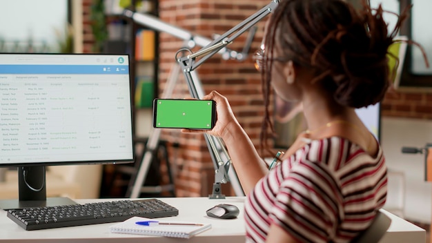 Afroamerikanischer Freiberufler mit horizontalem Greenscreen auf dem Handy, Blick auf isolierte Mockup-Vorlage mit Chroma-Key-Hintergrund und leerem Copyspace. Smartphone halten.