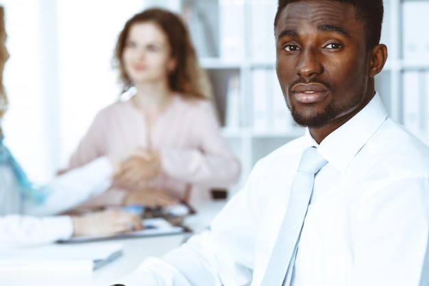 Afroamerikanischer Geschäftsmann bei einem Treffen im Büro, weiß gefärbt. Multiethnische Gruppe von Geschäftsleuten.