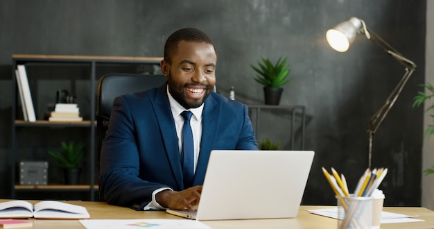 Afroamerikanischer Geschäftsmann, der am Tisch sitzt und Videochat auf Laptop-Computer hat.