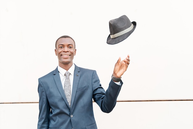 Afroamerikanischer Geschäftsmann, der einen Hut auf einen weißen Steinhintergrund wirft