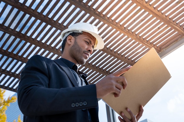 Afroamerikanischer Geschäftsmann-Manager mit Bauhelm, der Blaupausen für ein Projekt überprüft