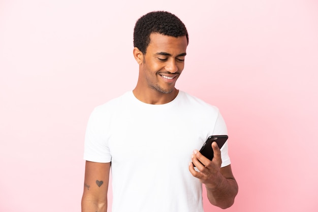 Afroamerikanischer gutaussehender Mann auf isoliertem rosa Hintergrund, der eine Nachricht oder E-Mail mit dem Handy sendet sending