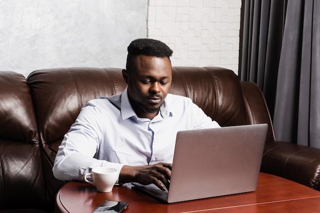 Afroamerikanischer IT-Entwickler mit Laptop programmiert Code im Büro Afrikanischer Geschäftsmann arbeitet am Laptop und chattet mit Kollegen