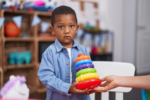 Afroamerikanischer Junge hält einen Plastikturm aus Reifenspielzeug im Kindergarten