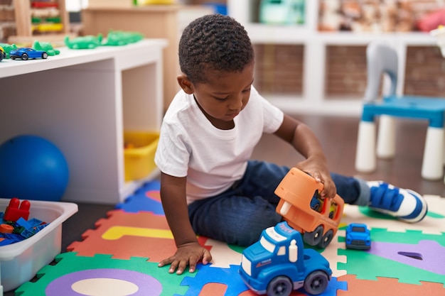 Afroamerikanischer Junge spielt mit Autos und LKW-Spielzeug, das im Kindergarten auf dem Boden sitzt