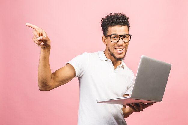 Afroamerikanischer junger Mann, der Laptop über lokalisiertem rosa Hintergrund verwendet, überrascht