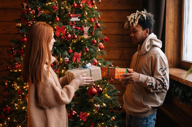 Afroamerikanischer junger Mann und kaukasische junge Frau, die sich im festlichen Raum Weihnachten schenken